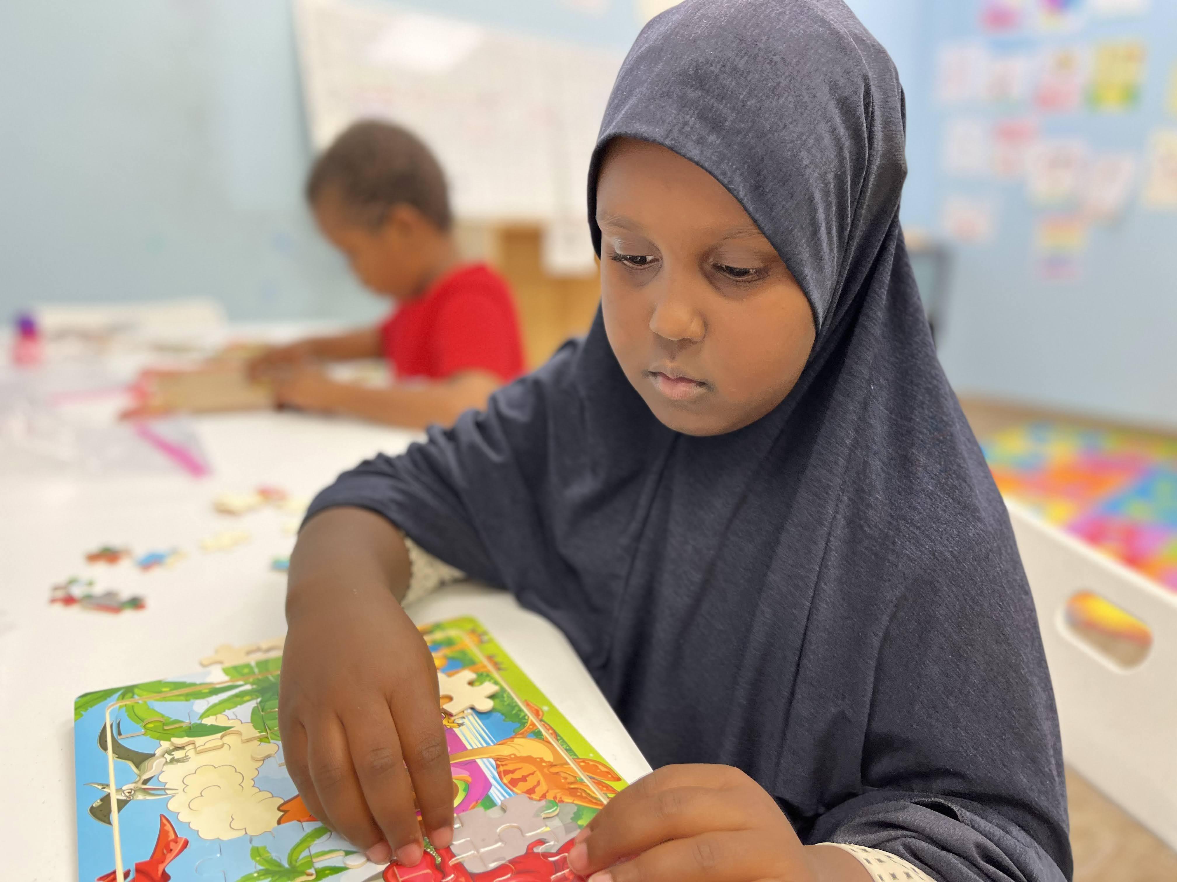 A girl wearing a hijab works on a project at school.